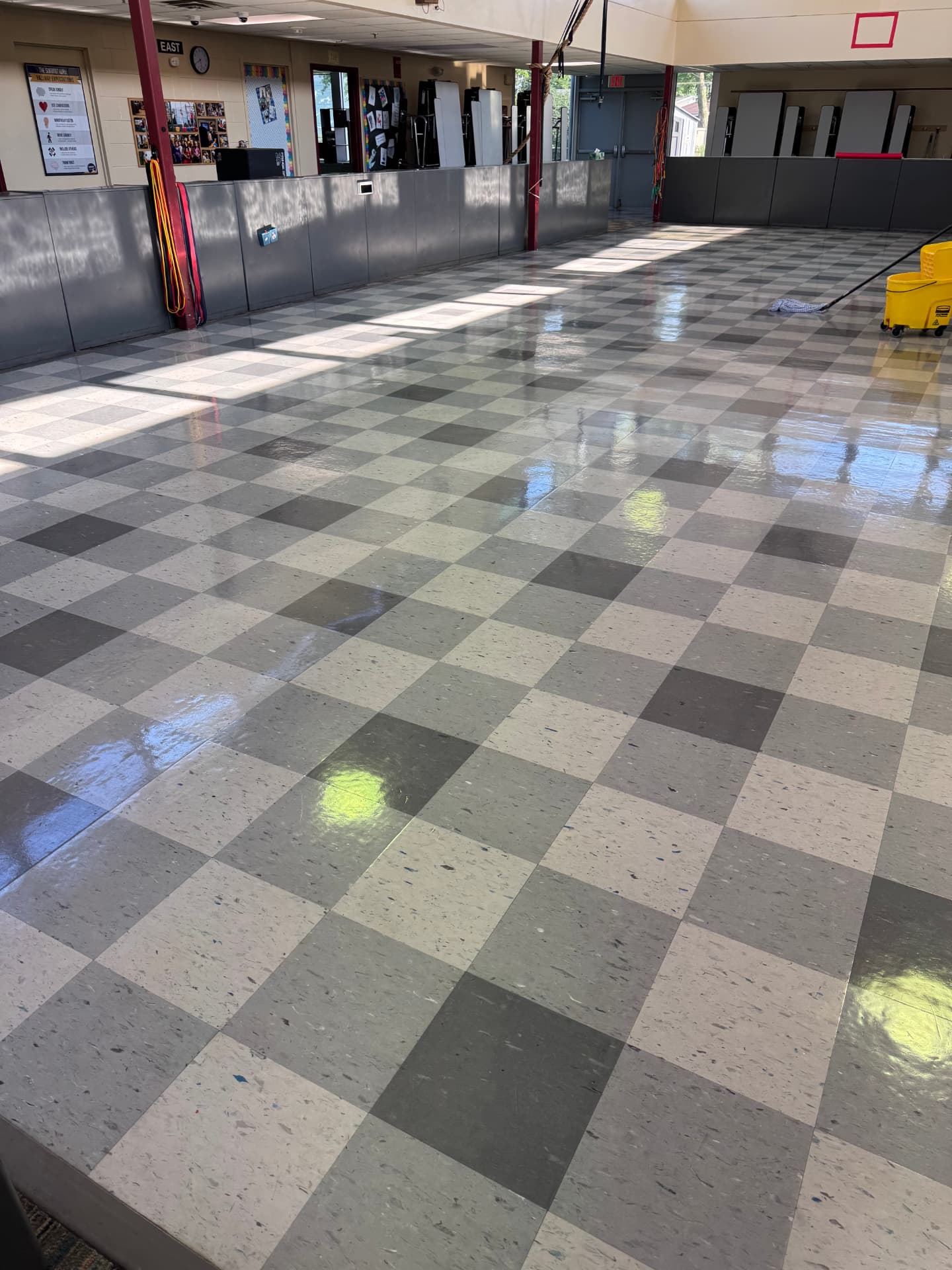 Mop and yellow mop bucket on a glossy cleaned floor in a school gymnasium