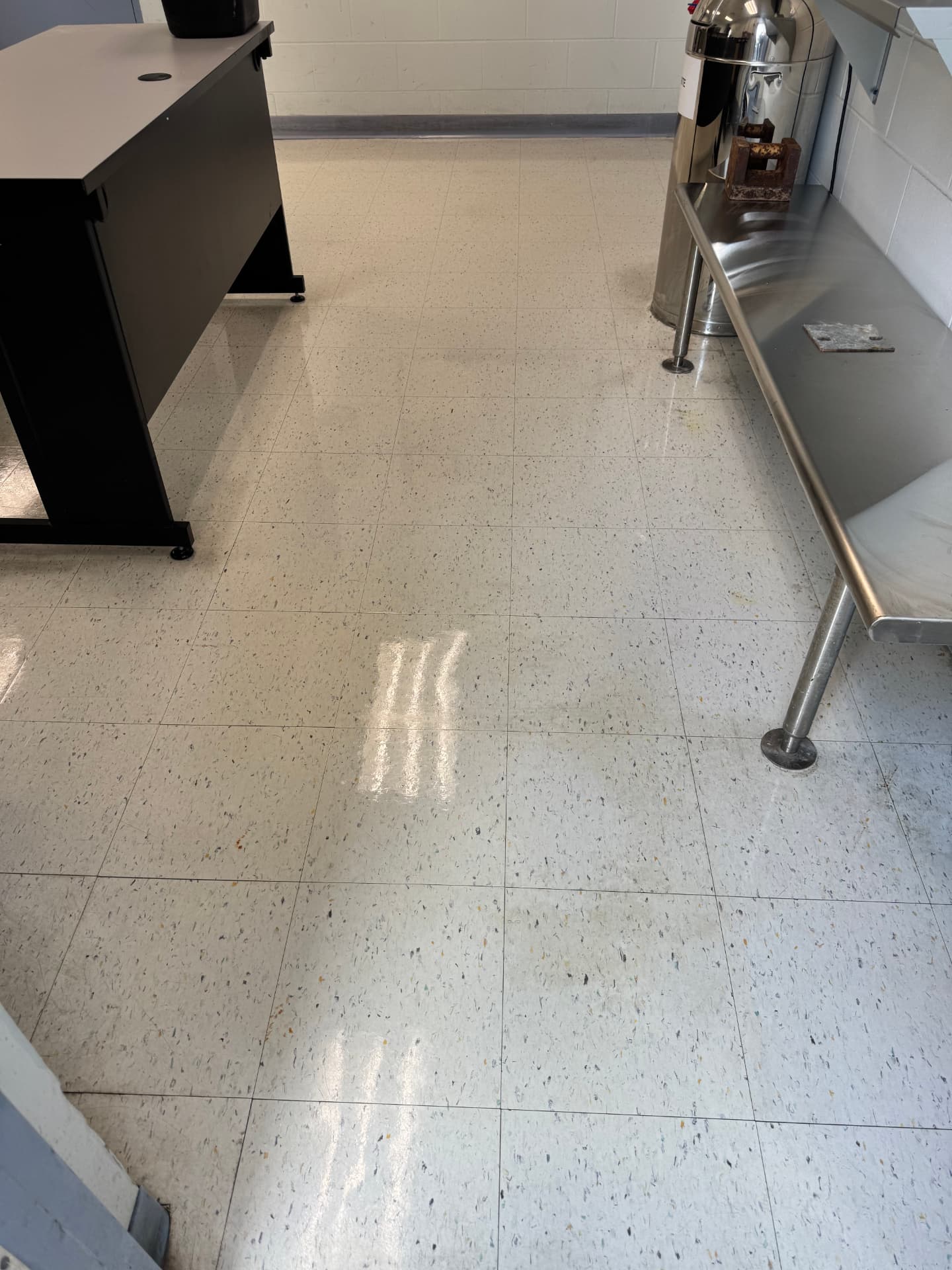 Freshly cleaned floor beside a stainless steel bench in a facility workroom