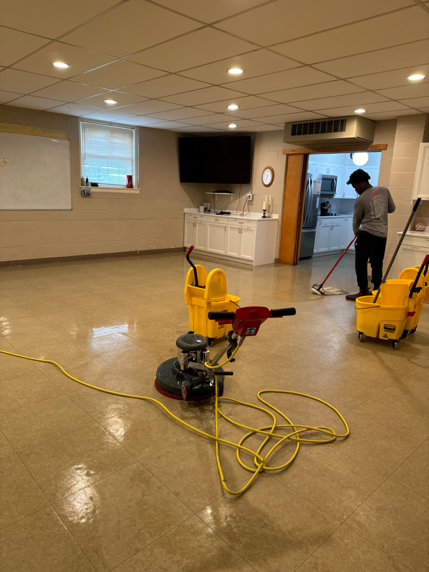 Team member mopping beside a floor machine in a meeting hall