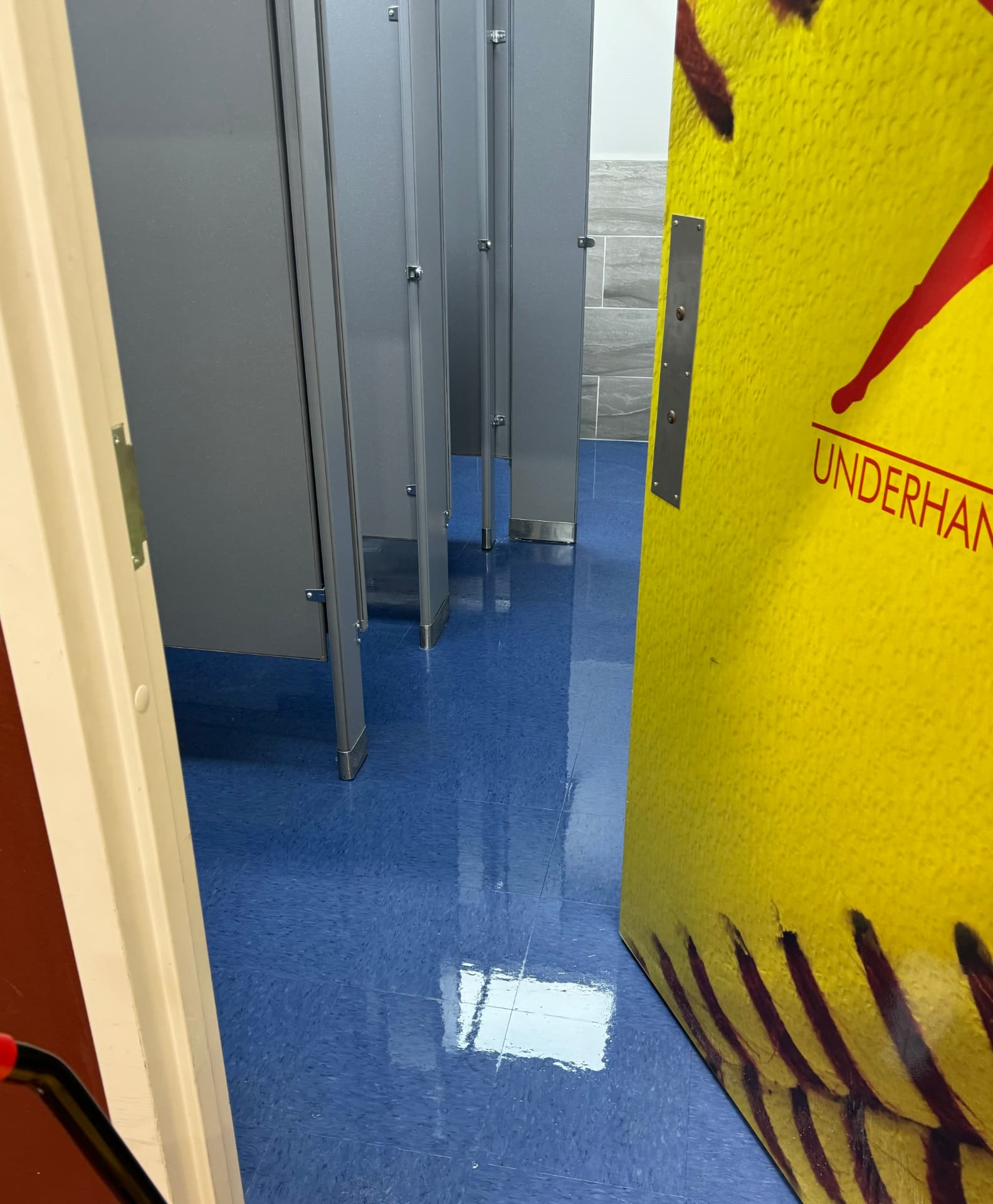 Clean, glossy blue tile floor of a facility restroom seen between the stalls